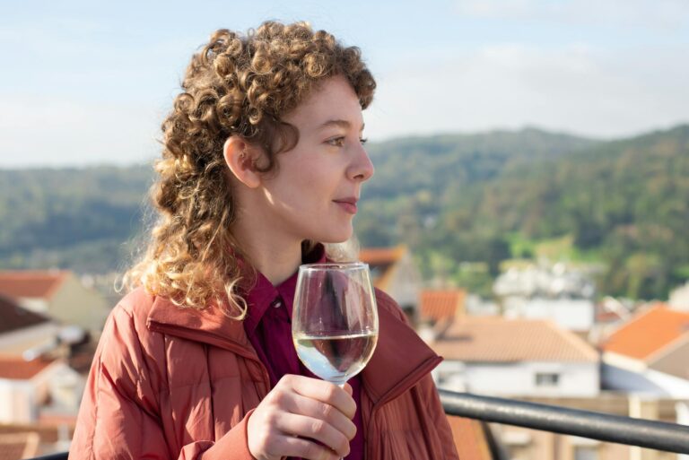 Profile of a woman holding a wine glass on a balcony with scenic Portugal landscape.